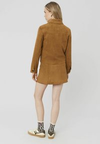 Veste en daim marron au design ajusté, avec des manches à boutons et une jupe assortie. Baskets blanches aux accents marron et chaussettes imprimées léopard.