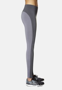 Szare legginsy sportowe z wysokim pasem, gładką teksturą oraz ciemniejszymi bocznymi panelami. Do tego czarne buty sportowe.