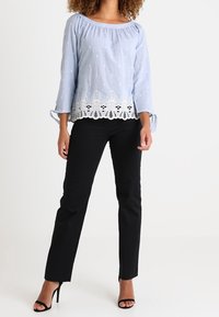 Blouse bleu clair avec un col froncé, des manches 3/4 et une bordure en dentelle blanche à l'ourlet, associée à un pantalon noir ajusté et des talons hauts.