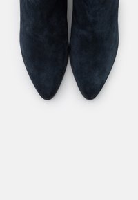 Stivaletti in suede blu navy, con un design a punta e una texture liscia. Le suole sono piatte con una leggera curvatura al tallone.