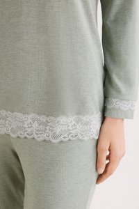 Ljusgrön avslappningsklädsel med spetsdetaljer vid ärmarna och fållen, med en mjuk textur och avslappnad passform. Synlig hand som håller i tyget.