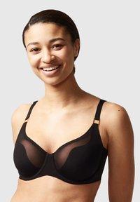 Black underwire bra featuring sheer mesh panels, adjustable straps, and gold-tone hardware accents. Smooth fabric with a molded cup shape.