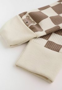 Beige and brown checkered ribbed fabric with bear face pattern and solid beige folded cuffs of a long-sleeve garment.