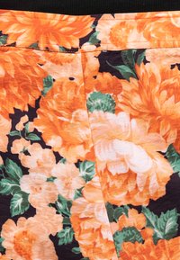 Ύφασμα με ζωηρό φλοράλ μοτίβο που περιλαμβάνει μεγάλα πορτοκαλί και λευκά λουλούδια με πράσινα φύλλα σε μαύρο φόντο.