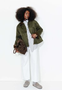 Veste vert olive avec des accents marron ; chemise rayée bleu clair ; pantalon large blanc ; sac fourre-tout marron ; chaussures à enfiler en léopard gris.