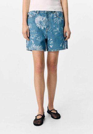 Ljusblå denimshorts med blommönster, hög midja och uppvikta fållar, tillsammans med svarta mesh-skor.