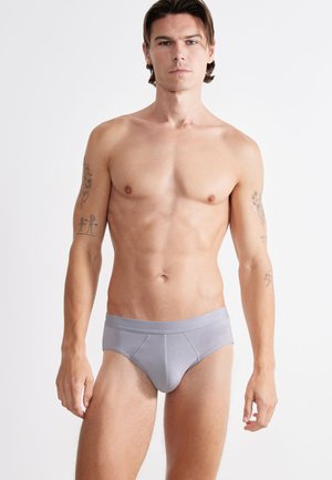 Slip da uomo grigio a vita bassa realizzato in tessuto morbido. Caratterizzato da un ampio elastico in vita, cuciture nel pannello anteriore e una silhouette aderente. Branding ridotto e discreto.