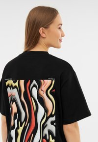 Černé oversized tričko s vícerozměrným abstraktním grafickým designem na zádech, s hladkými texturami a zakřivenými tvary.