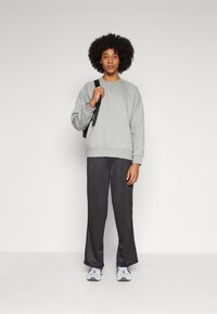 Grau Sweatshirt mit Rippbündchen, kombiniert mit dunkelgrauen, weiten Hosen und hellgrauen Sportschuhen. Schwarzer Rucksack über einer Schulter getragen.