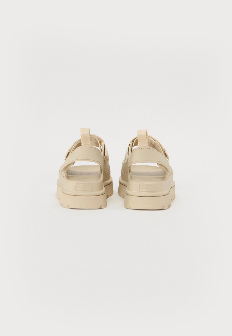 Beige Sandalen mit dicker Sohle, offenem Absatz und Riemen über dem Fuß. Texturiertes Obermaterial mit einer Schlaufenstoffdetail für einfaches Anziehen.