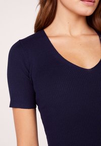 Navy ribbed top featuring a V-neckline and short sleeves. The texture is smooth with a fitted design that outlines the neckline and shoulders.