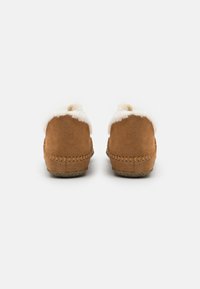 Chaussons en suède beige avec un intérieur en fausse fourrure blanche au niveau du col. Détails brodés le long du bord et semelle en caoutchouc texturée.
