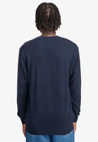 Dunkelblauer Pullover mit Rundhalsausschnitt, gerippten Bündchen und Saum, der eine glatte Textur und eine lockere Passform aufweist.