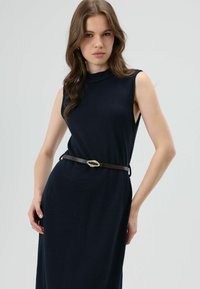 Mouwloze marineblauwe jurk van gestructureerde stof, met een hoge halslijn en een bruine riem met een decoratieve gouden gesp.