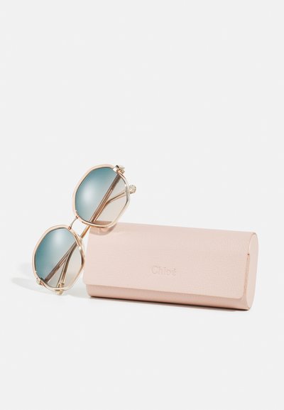 Occhiali da sole con montatura dorata e lenti sfumate blu appoggiati su un astuccio in pelle rosa pallido Chloé.