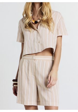 Kvinde iført beige og hvide vertikale stribede crop top med korte ærmer og matchende højtaljede shorts, med chunky halskæder og armbånd.