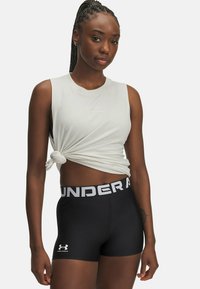 Lichtgrijs mouwloos topje met knoopdetail, gecombineerd met zwarte strakke shorts met een witte logoband en een klein logo op het been.