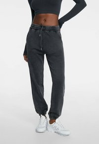 Donkergrijze joggingbroek met elastische tailleband en enkelmanchetten. Gemaakt van zacht materiaal. Gecombineerd met witte sneakers voor contrast.