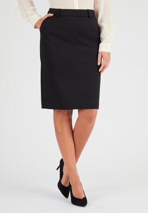 Jupe crayon noire, longueur genou, en tissu lisse avec une taille élastique et des poches latérales, portée avec des chaussures à talons hauts noires.
