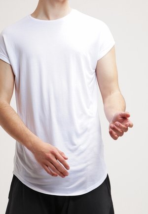 Person iført en ensfarvet hvid kortærmet t-shirt og sorte bukser, med let bøjede arme og hænder hævet foran.