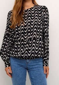 Czarna i biała bluzka z długim rękawem w faliste wzory, wykonana z miękkiego materiału, w połączeniu z jasnoniebieskimi dżinsami.