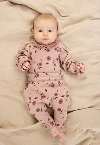 Rózsaszín virágmintás öltözet fodros nyakkivágással és mandzsettákkal. Puha anyagból készült, apró virágokkal és levelekkel díszítve.