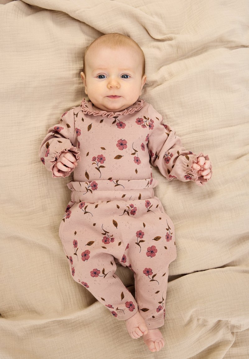 Rózsaszín virágmintás öltözet fodros nyakkivágással és mandzsettákkal. Puha anyagból készült, apró virágokkal és levelekkel díszítve.