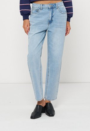 Femme portant un jean droit taille haute bleu clair, associé à des chaussures noires fermées slip-on et un pull court bleu marine.