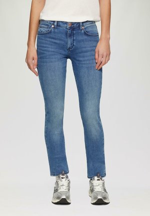 Blaue Denim-Jeans mit schlanker Passform, Fünf-Taschen-Design und subtilen Verwaschungen. Kombiniert mit metallisch silbernen Sneakern.