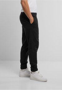 Zwarte sweatpants met een elastische tailleband, zijzakken en taps toelopende manchetten, gecombineerd met witte sneakers. Gladde stoftextuur.
