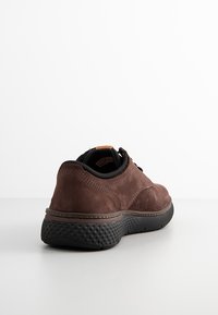 Brązowe zamszowe sneakersy z wyściełanym kołnierzem, czarną gumową podeszwą, kontrastującym przeszyciem i teksturowanym tyłem dla lepszej przyczepności.