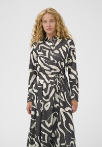 Langärmliges Kleid in Schwarz mit einem weißen abstrakten Muster, aus glattem Stoff; verfügt über einen Kragen und ein gebundenes Taillendetail.