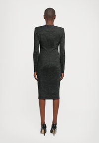 Long-sleeve black dress with a fitted silhouette, textured fabric, and knee-length hem. Worn with black high-heeled shoes.