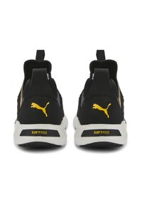 Zwarte sportieve schoenen met een zachte textiele bovenkant, contrasterend gele logo en een gewatteerde witte zool. Beschikken over trekbanden bij de hiel voor gemakkelijk aan- en uittrekken.