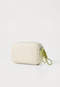 Pochette beige en matériau lisse, dotée d'une fermeture éclair argentée et d'accents en cordon tordu vert. Forme rectangulaire avec des bords arrondis.