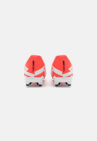 Scarpe da calcio rosse e bianche con design aerodinamico, parte superiore testurizzata e dettagli neri sul tallone e sul logo. Suola con tacchetti per la trazione.
