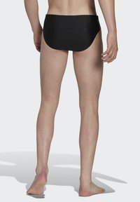 Slips de bain noirs avec une texture lisse et un ajustement serré. Le design présente une taille basse et aucun motif ou accent supplémentaire.