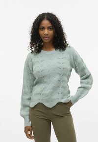 Mintgrön stickad tröja med vågmönster, ribbade ärmslut och scalloped fåll. Matchad med olivgröna åtsittande byxor.