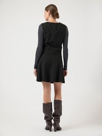 Musta hihaton mekko, jossa on vartalonmyötäinen yläosa ja liehukehelma. Harmaa pitkähihaisen paita alla. Ruskeat polven yli ulottuvat nilkkurit korkokengillä.