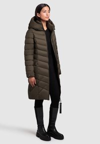 Garšs olīvzaļš pūkains mētelis ar kapuci, ar diagonālu dūkoņu, priekšējo rāvējslēdzēju un sānu kabatām. Nēsāts ar melnām augstiem zābakiem.