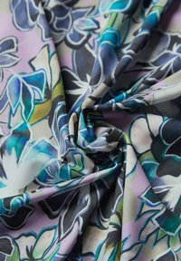 Blumenerstoff mit einem wirbelnden Design in Blau-, Grün- und Lilatönen auf einem hellen Hintergrund, gekennzeichnet durch filigrane Blumenmuster und eine glatte Textur.