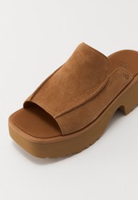 Bruine suède slide sandaal met open teen, dikke gevoerde zool en taps toelopend bovenwerk. Voorzien van een duurzame buitenzool voor grip.
