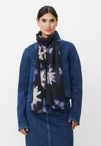 Czarny szalik w kwiatowe wzory w kremowych i fioletowych odcieniach, wykończony postrzępionymi brzegami, noszony na dżinsowej kurtce.