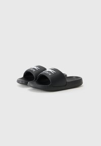 Black slide sandals made of smooth synthetic material, featuring a wide strap with a white logo and a textured footbed for grip.