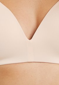 Reggiseno beige chiaro con scollatura a V profonda, texture a costine, costruzione senza cuciture e stile minimalista, che mette in risalto il tessuto liscio.