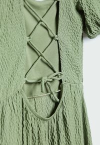 Robe verte en tissu texturé, dotée d'un décolleté rond et d'un dos croisé maintenu par des liens.