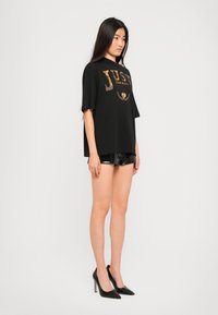 Black oversized t-shirt with a gold graphic print, paired with shiny black shorts and pointed stiletto heels. Smooth texture, casual design.