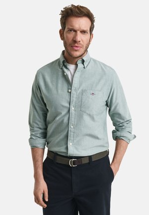 Lichtgroen overhemd met knopen en een zak, opgerolde mouwen en donkere broek, gecombineerd met een grijze riem met een zilveren gesp.