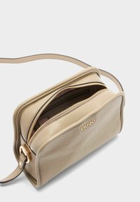 Beige leren schoudertas met een ritssluiting. Heeft een gestructureerd oppervlak en goudkleurige hardware. Gekentekend met "LIUJO" aan de voorkant.