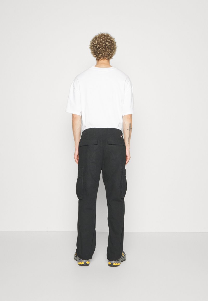 Pantaloni cargo neri con ampie tasche laterali, taglio dritto e tessuto texturizzato. Abbinati a una t-shirt bianca aderente.